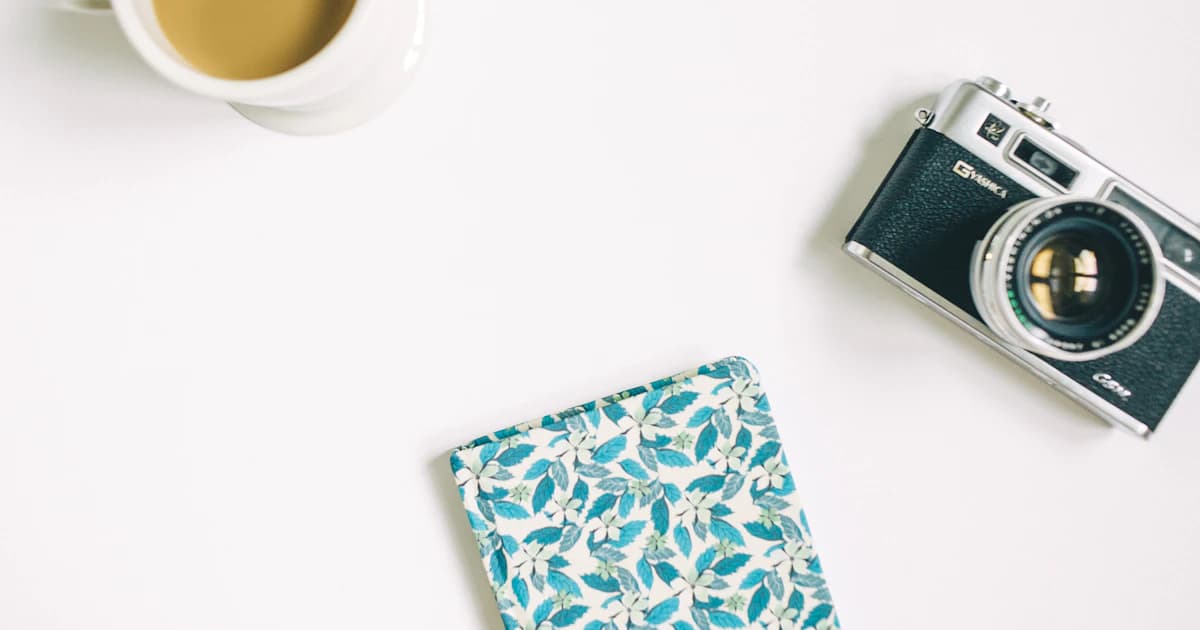 A camera, notebook and cup arranged on a white desktop