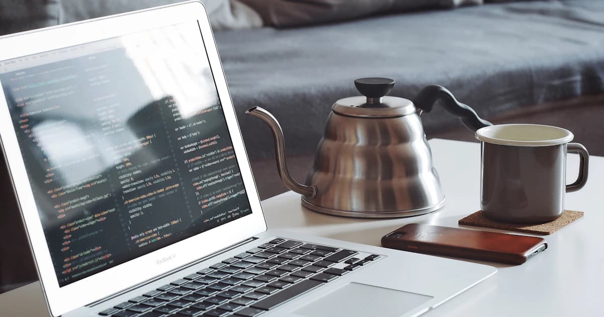 A laptop and metal teapot on a work table