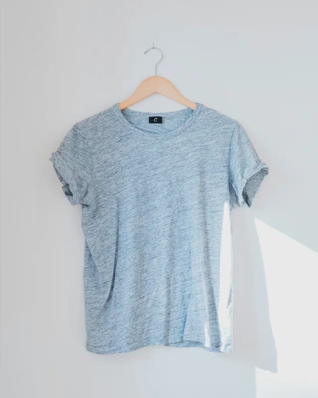 Heather blue tee on a hanger against a sunlit wall